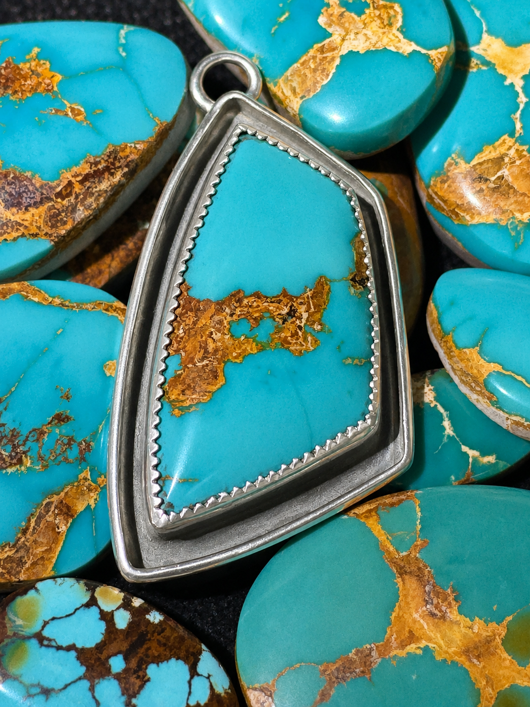 Finished Cradle to Grave turquoise pendant resting among hand-cut turquoise cabochons